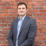 man in gray suit jacket standing beside brown brick wall